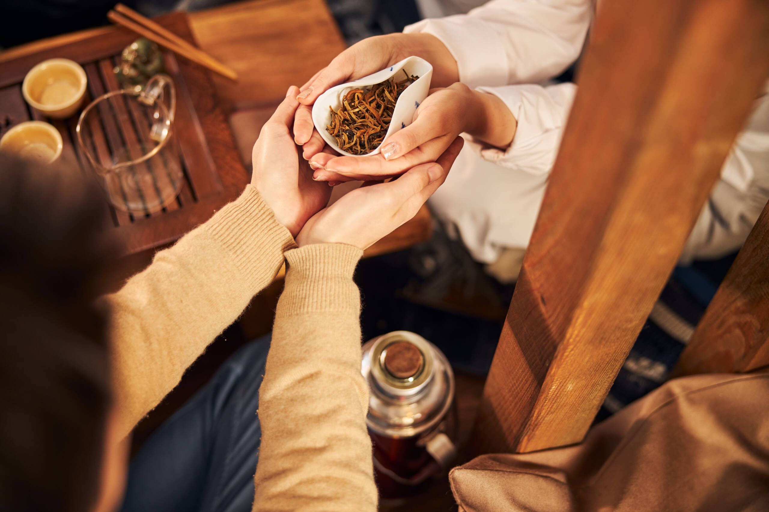Close up of young man holding woman hands with dry tea leaves while sitting at the table in tea house
