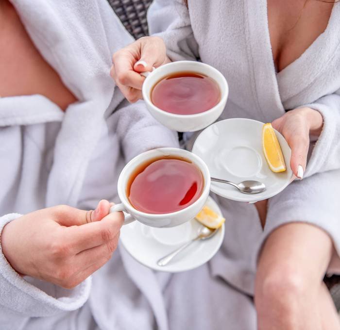 A couple in white bathrobes are sitting on an open terrace by the sea, drinking tea with lemon from cups. Lovers travel on vacation. Young man and woman hug each other. Newlyweds on their honeymoon A couple in white bathrobes are sitting on an open terrace by the sea, drinking tea with lemon from cups. Lovers travel on vacation. Young man and woman hug each other. Newlyweds on their honeymoon