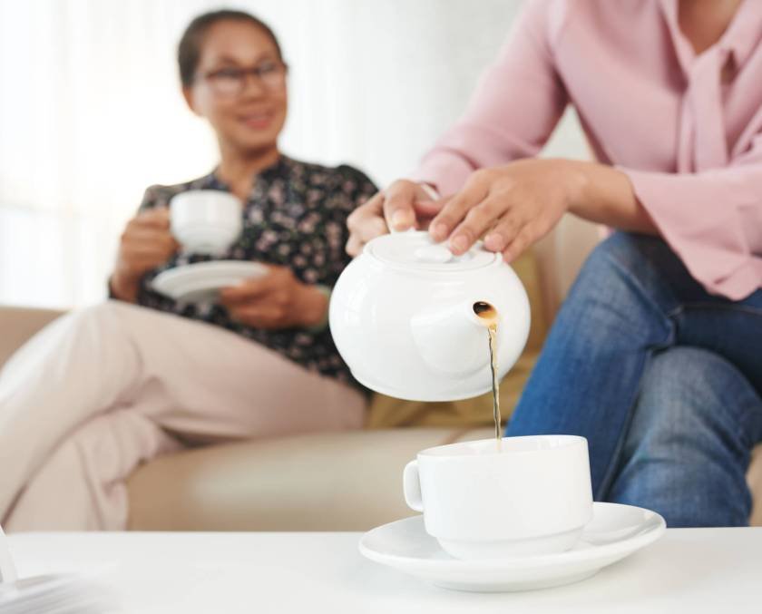 Filling cup with tea Woman pouring tea into porcelain cup when talking to her senior mother