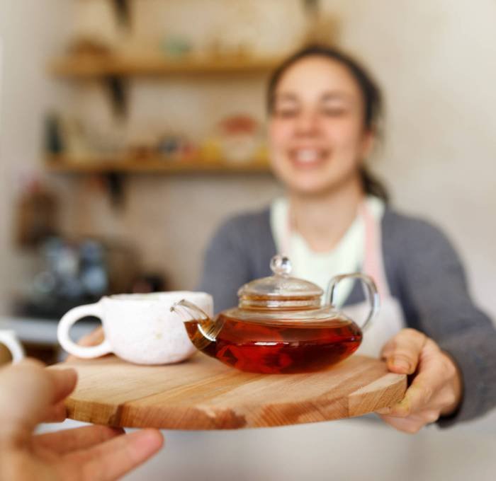 Happy young woman in apron, startup come true. Small business concept. Family business, cafe place. Giving orders, holding tea tray and cup, close up Happy young woman in apron, startup come true. Small business concept. Family business, cafe place. Giving orders, holding tea tray and cup, close up.